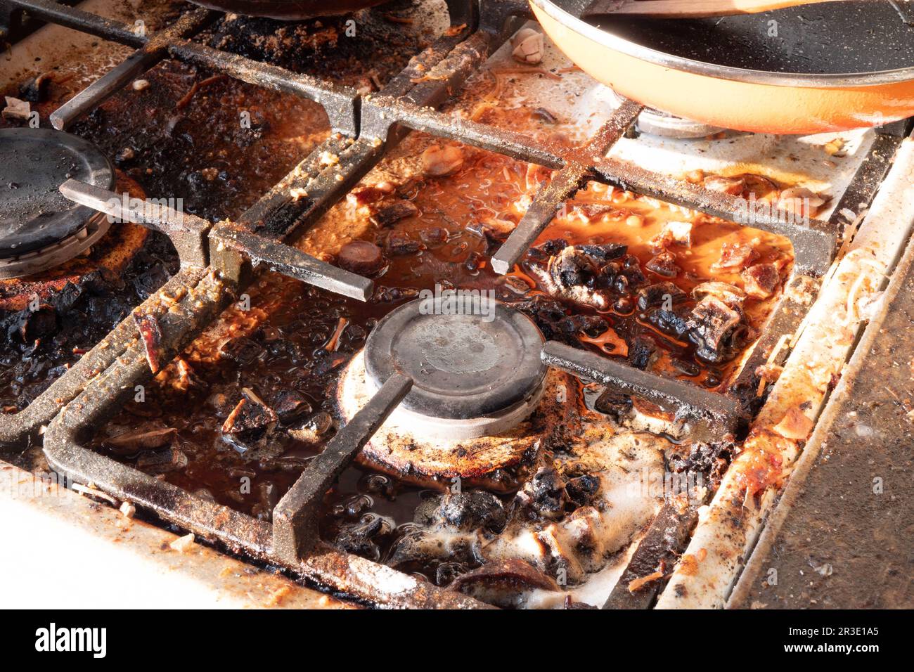 Superficie stufa a gas sporca. Bruciatore a gas medio e griglia di ghisa di un forno a gas circondato da vecchi avanzi di cibo e bevande. Superficie dell'area superiore e bruciatura Foto Stock