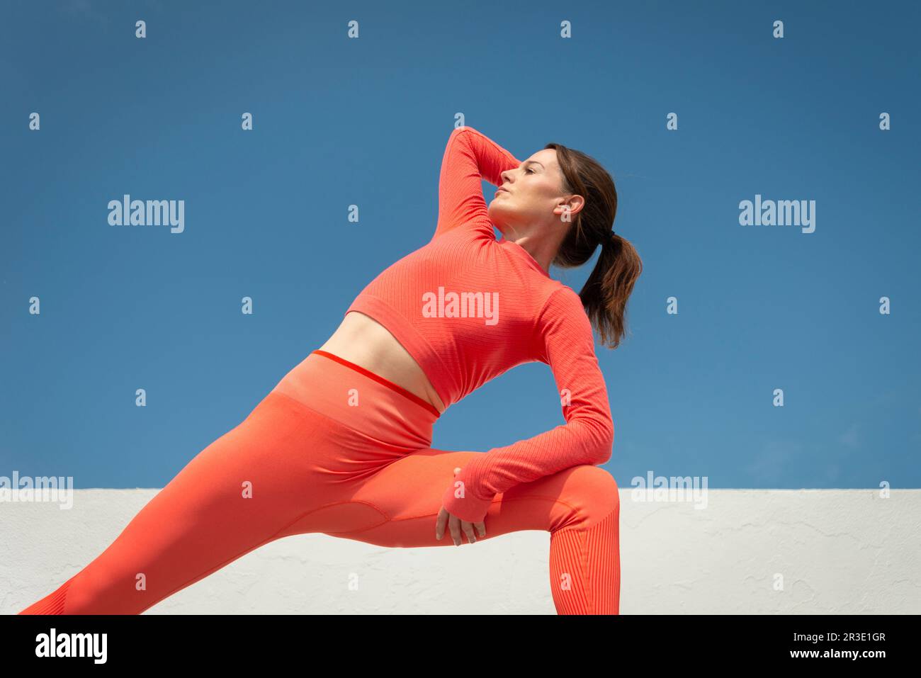 Atleta sana facendo allenamento fitness e stretching fuori da una parete bianca, cielo blu. Foto Stock