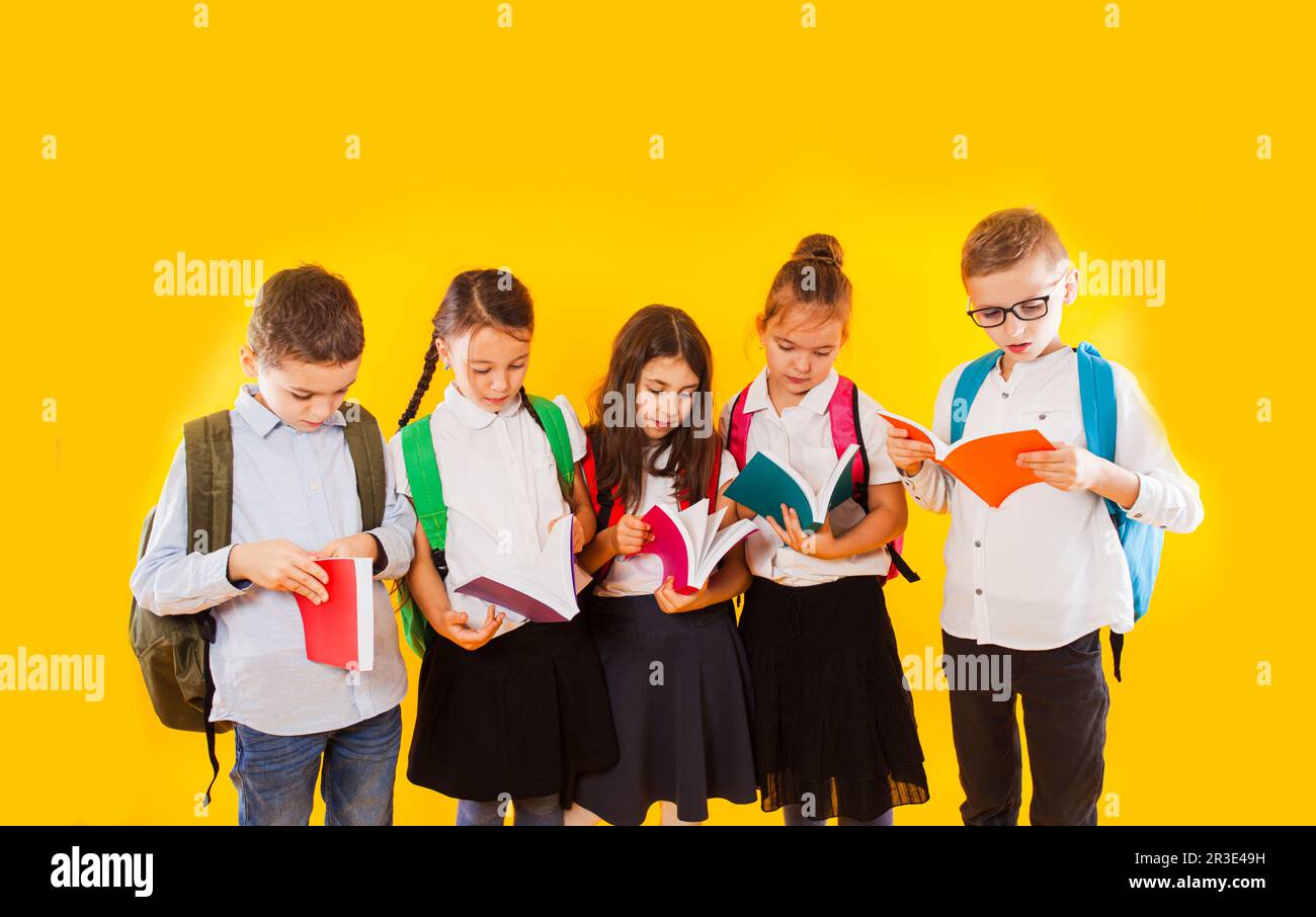 Felice eccitato sorridente piccoli studenti che tengono libri a colori isolati su sfondo giallo. Ritorno a scuola. Foto Stock