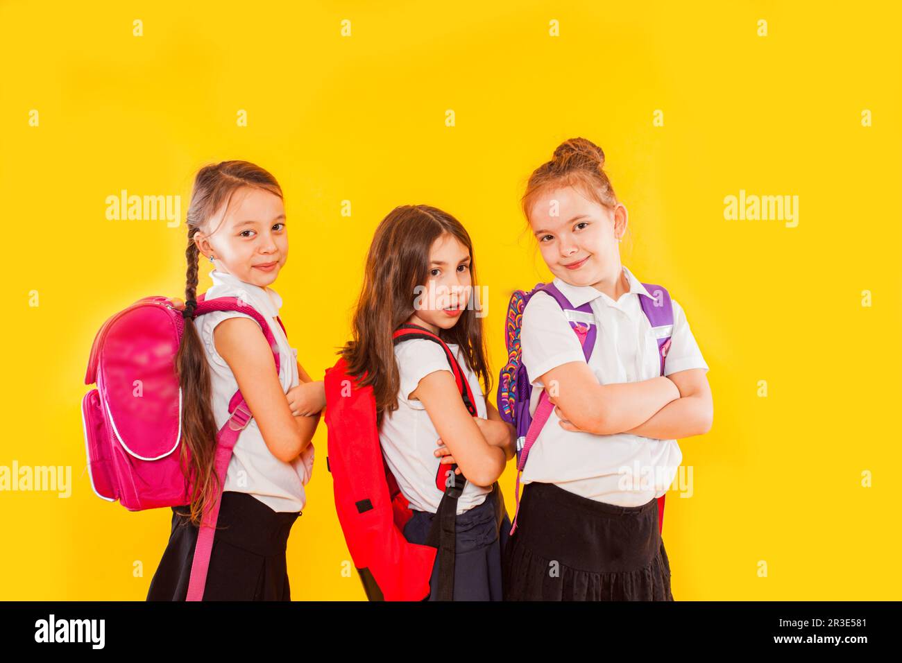 Ragazze carine in uniforme con zaini su sfondo giallo Foto Stock