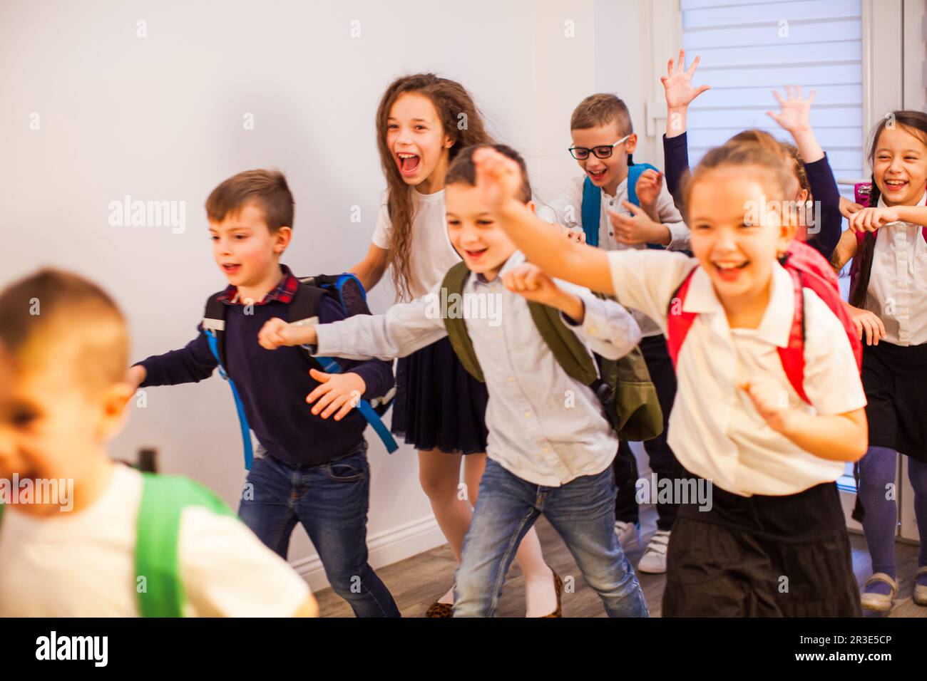 Bambini della scuola felice che corrono nel corridoio della scuola elementare, vista frontale Foto Stock