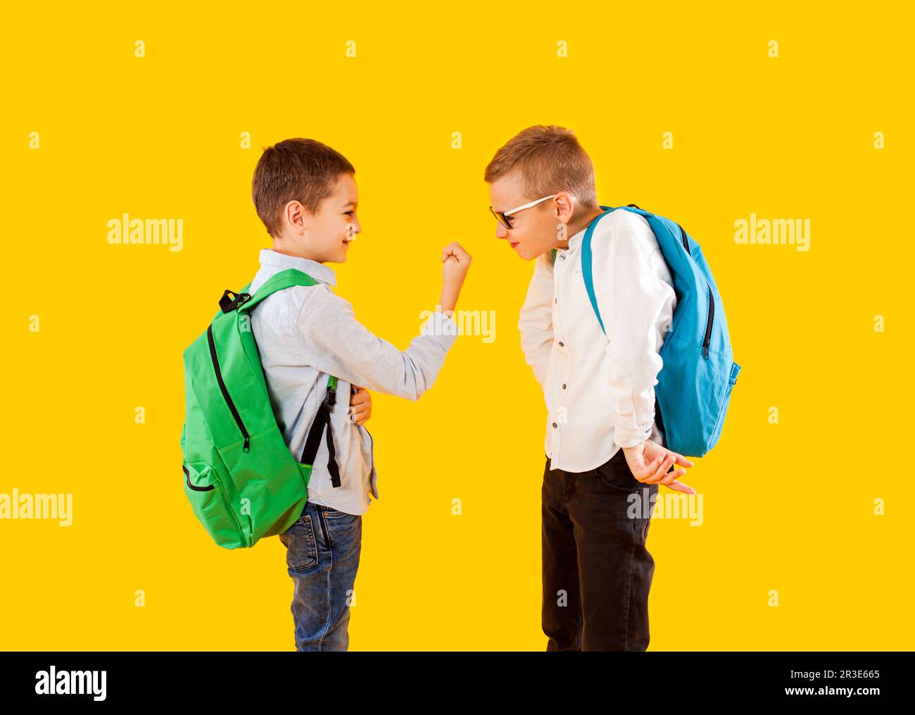 Graziosi scolari in uniforme con zaini su sfondo giallo Foto Stock