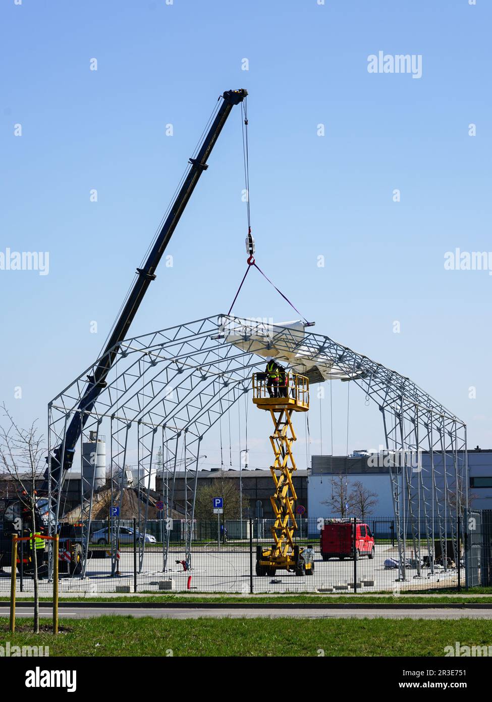 Installazione di una copertura in tessuto di cloruro di polivinile per l'hangar della tenda con telaio in metallo mediante gru telescopica e sollevatore a forbice semovente Foto Stock