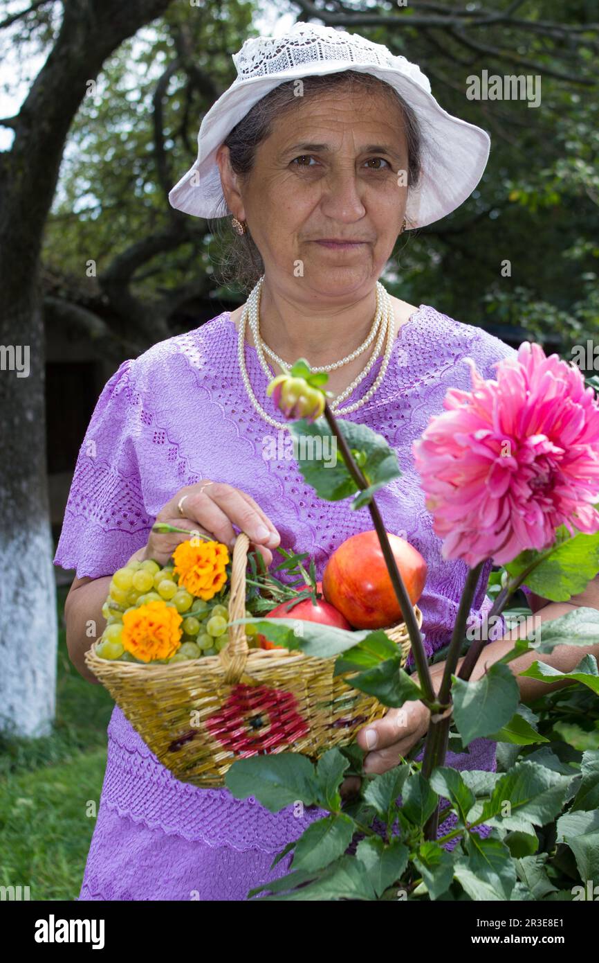 nonna in estate in giardino con cesto di frutta vicino al fiore Foto Stock