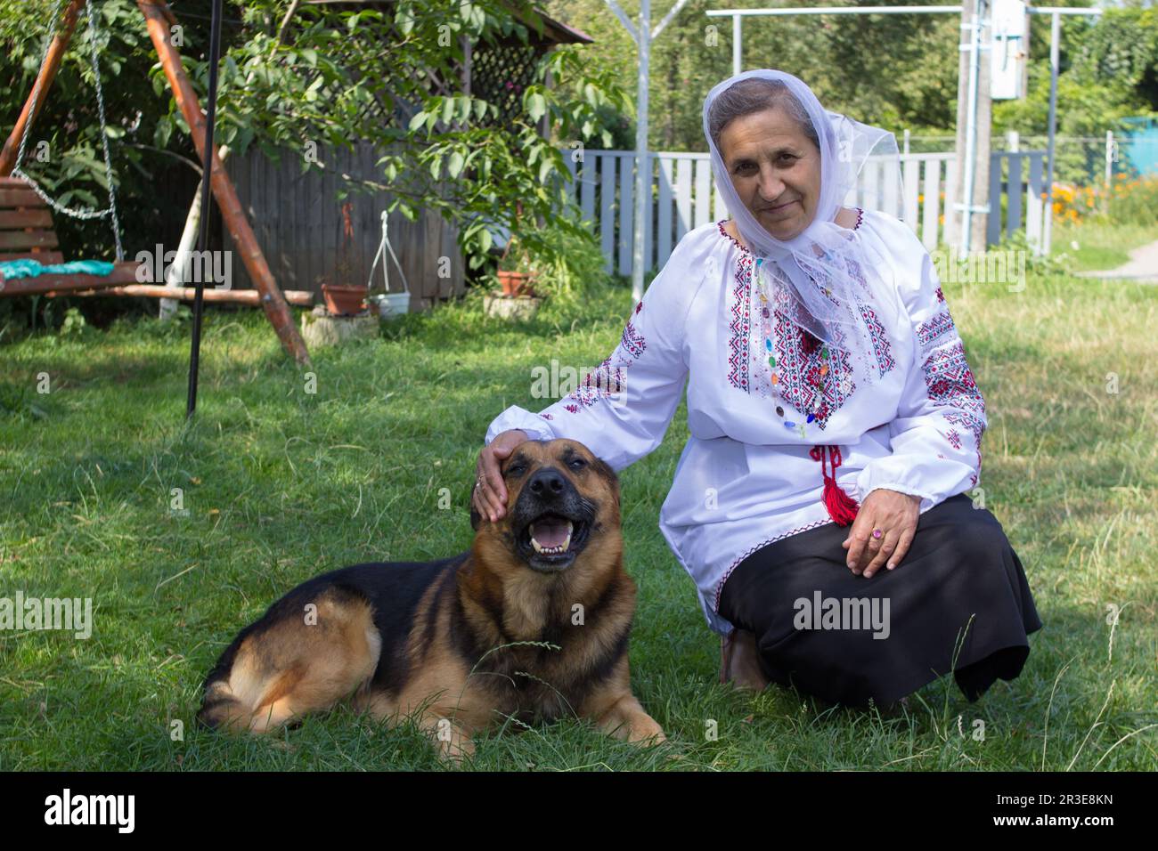 la donna di pensione si siede con il cane sull'erba in camicia ricamata Foto Stock