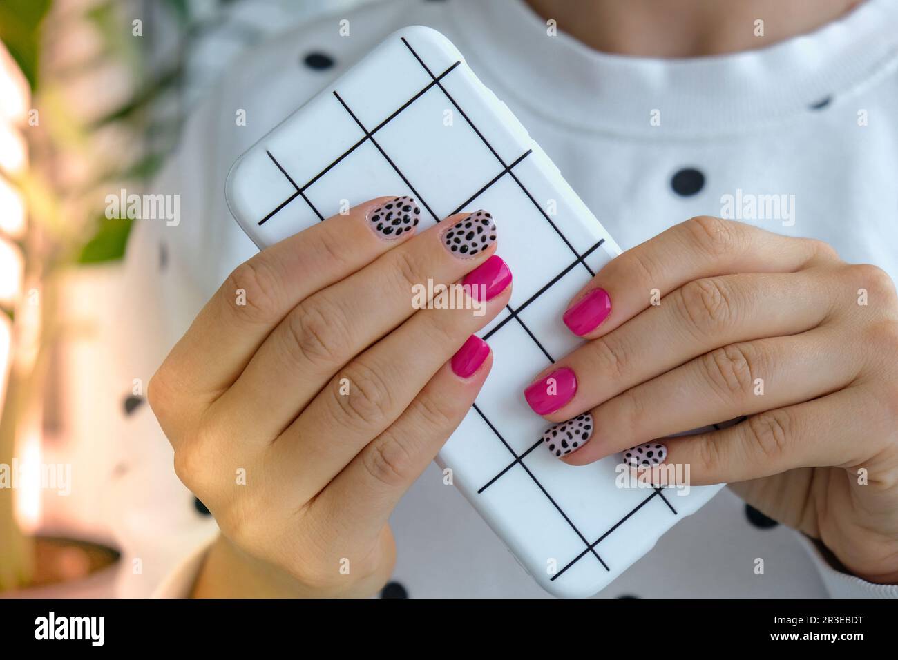 Mani femminili curate con eleganti chiodi rosa che tengono il telefono cellulare. Tecnologia smartphone. Manicure di design moderno e alla moda. Gel n. Foto Stock