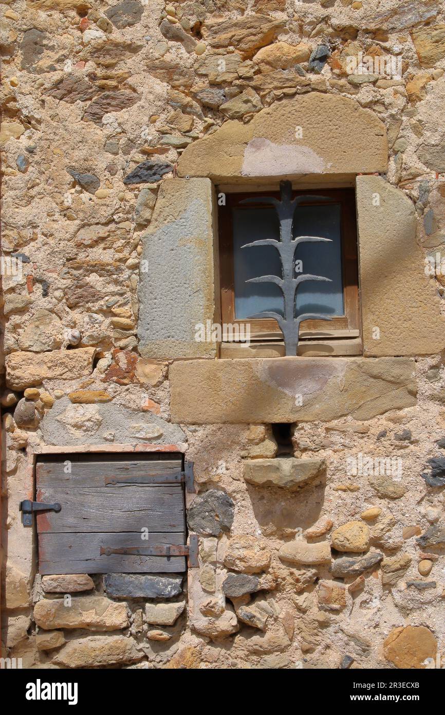 La foto è stata scattata nel villaggio spagnolo di Púbol, in provincia di Girona. La foto mostra un muro di pietra di una casa di paese con una piccola finestra Foto Stock