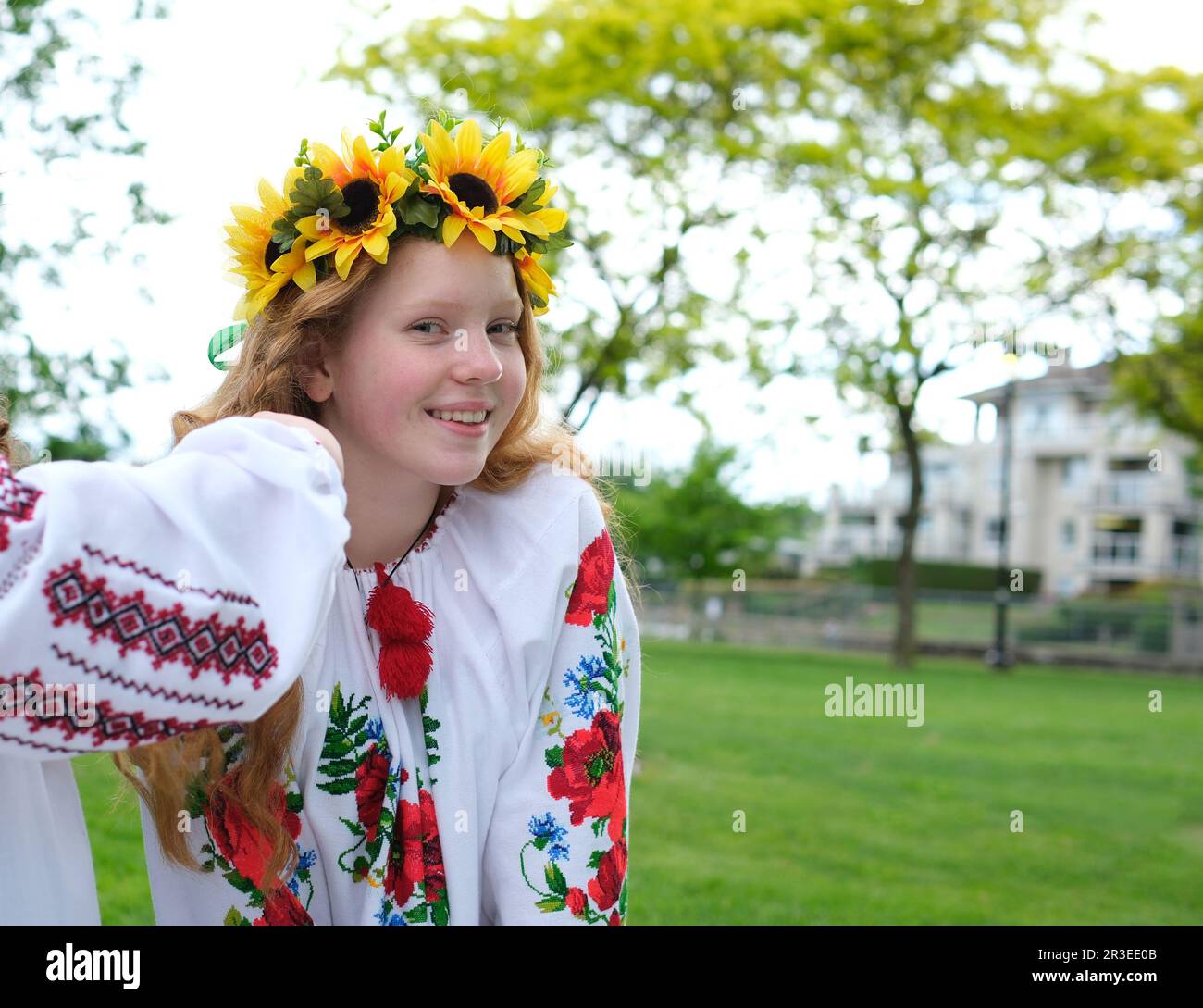 Ragazza soleggiato con capelli rossi luminosi si trova sullo sfondo di alberi verdi con corona di girasoli ricamati camicia nazionale donna Ucraina per la pace No guerra vittoria del patriottismo nazionale Ucraina Foto Stock