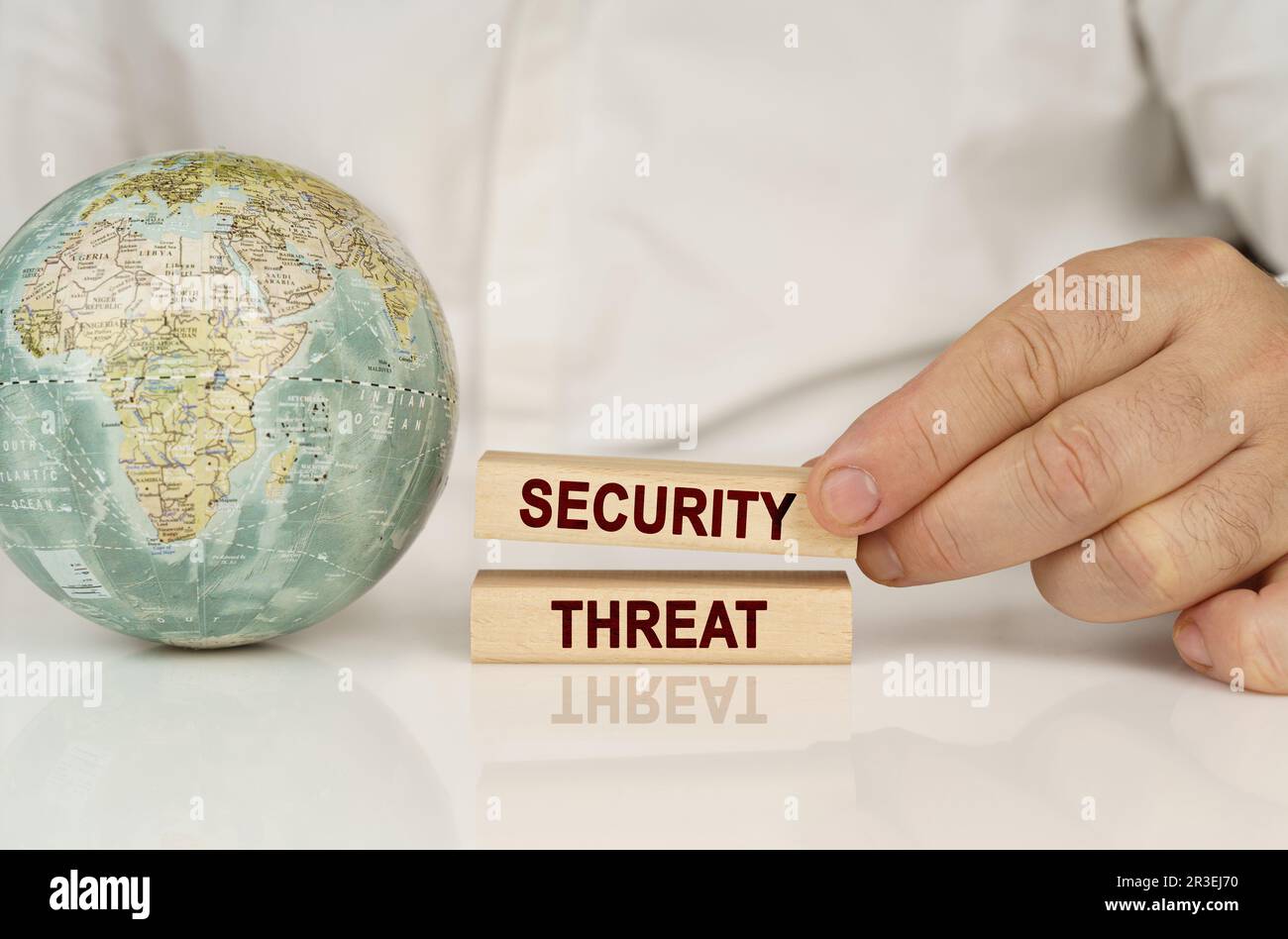 C'è un globo su una superficie bianca riflettente, nelle mani di blocchi di legno con l'iscrizione - minaccia di sicurezza. Foto Stock