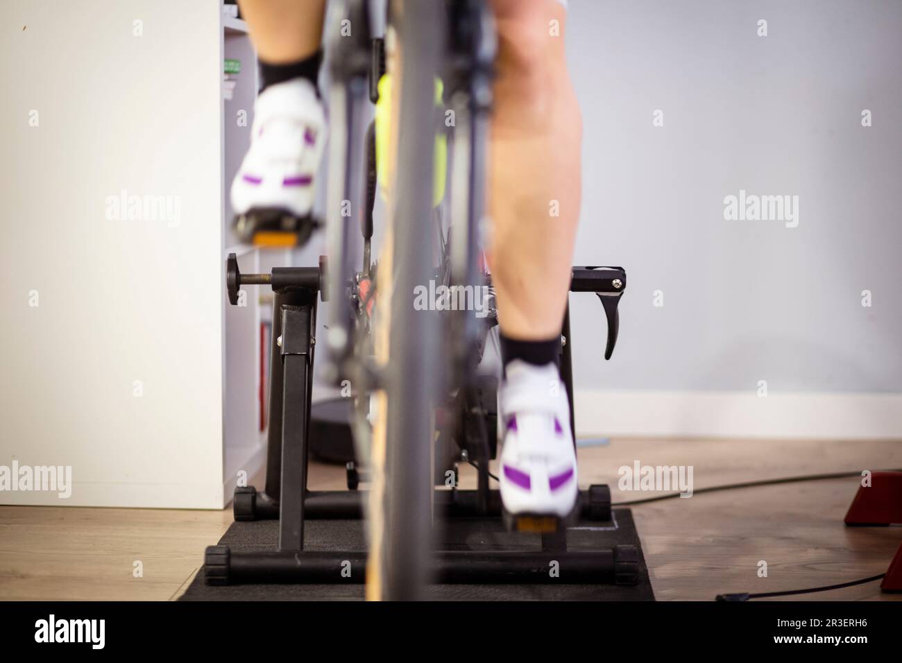 Due gambe pedalando una bicicletta in un allenatore al coperto in una casa domestica sport indoor tempo libero Foto Stock