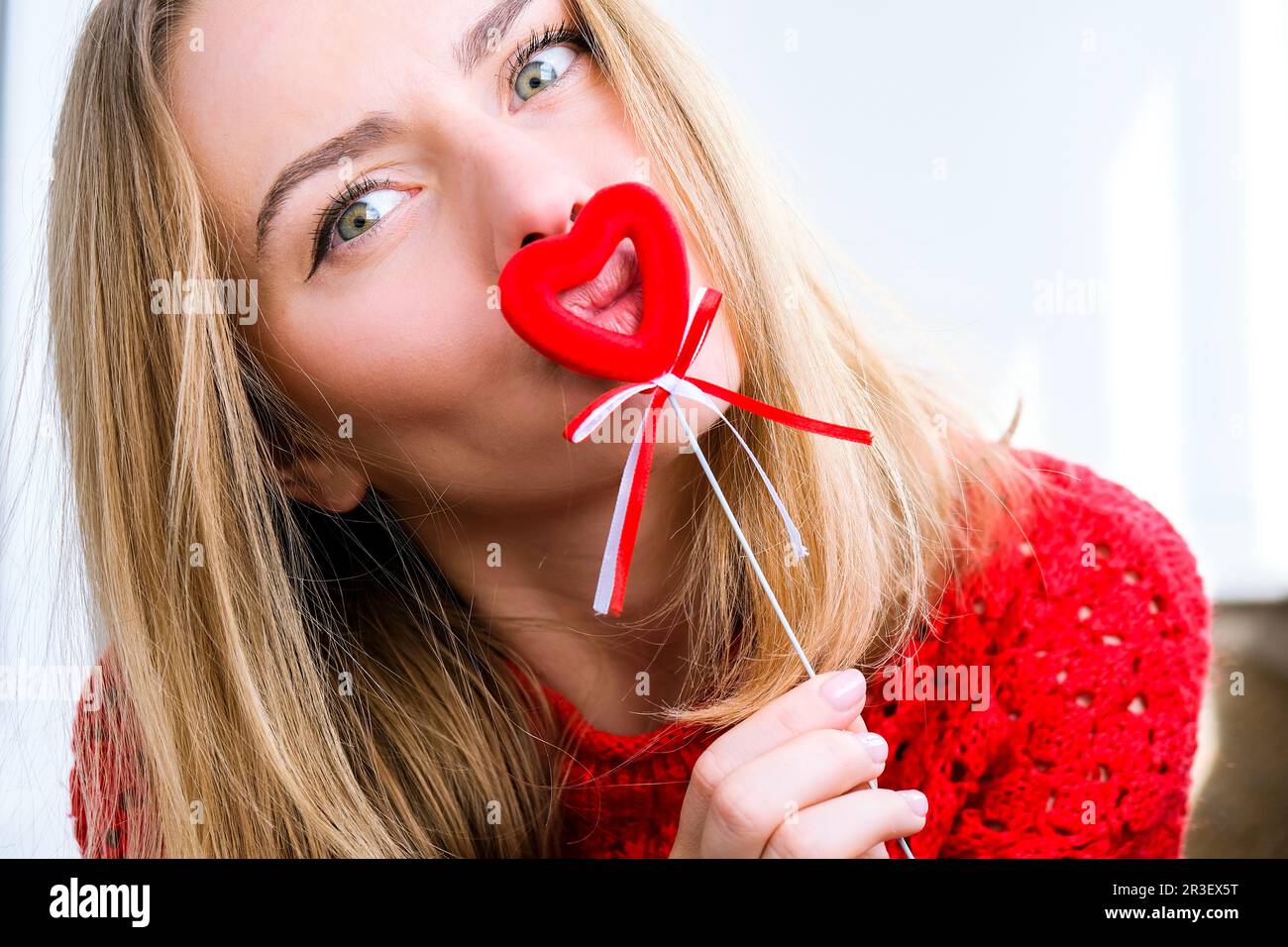 Giovane ragazza bionda in maglione rosso con cuori rossi che mostrano emozioni. Scattando selfie. San Valentino. Chat video. Amore in distanc Foto Stock