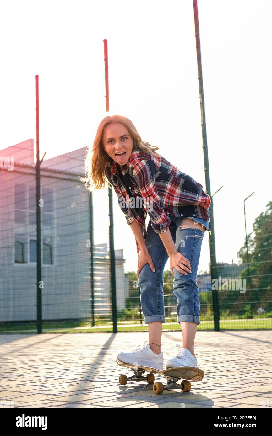 Donna in sella a uno skateboard per strada. Skater ragazza su un longboard. Cool femmina skateboarder al tramonto. Skater femminile spensierato 20s Foto Stock