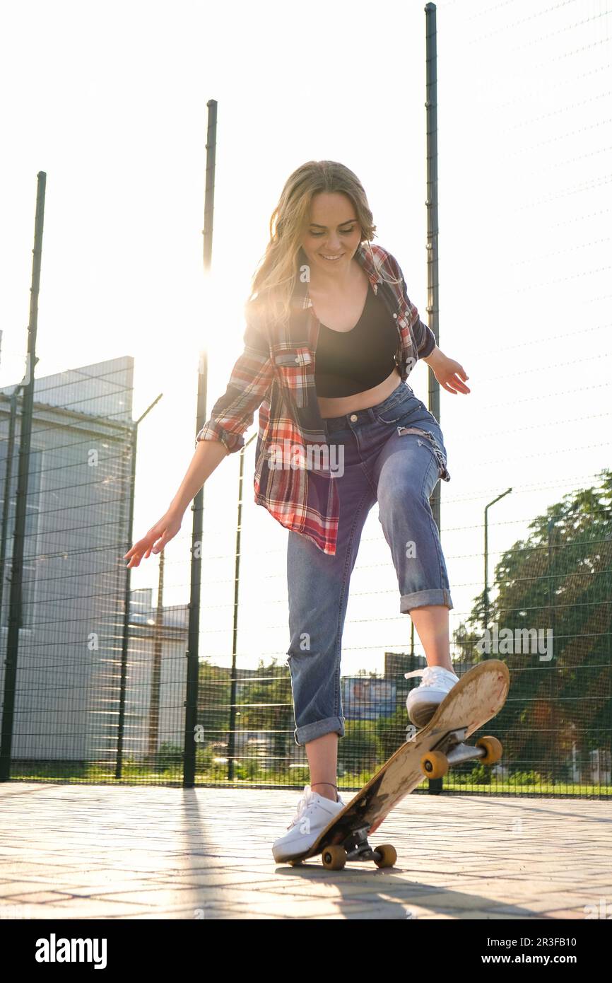 Donna in sella a uno skateboard per strada. Skater ragazza su un longboard. Cool femmina skateboarder al tramonto. Skater femminile spensierato 20s Foto Stock