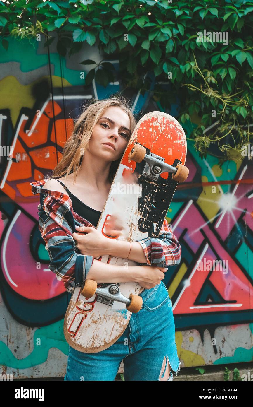 Donna in sella a uno skateboard su strade colorate Skater ragazza su un longboard. Cool femmina skateboarder al tramonto. Femminilità spensierata Foto Stock