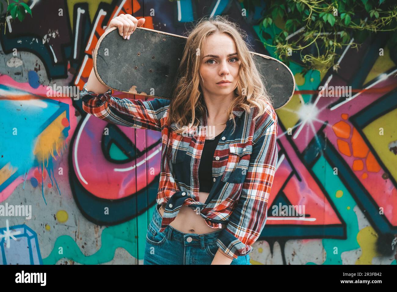 Donna in sella a uno skateboard su strade colorate Skater ragazza su un longboard. Cool femmina skateboarder al tramonto. Femminilità spensierata Foto Stock