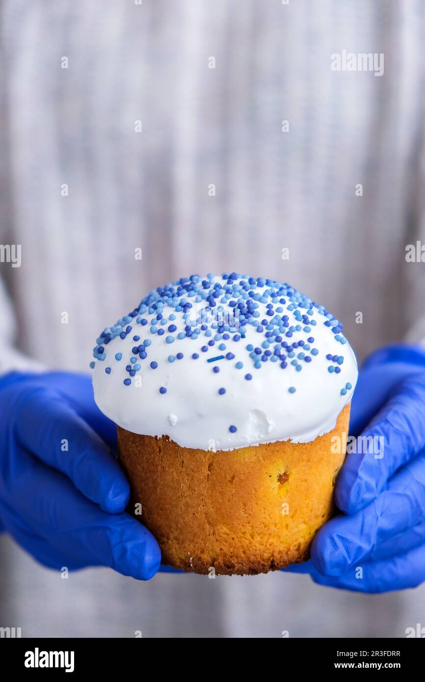 Mani in guanti blu tenere la torta di Pasqua con la guarnizione bianca e spruzzi blu. Donna con tradizionale torta di Pasqua russa. Casa Foto Stock
