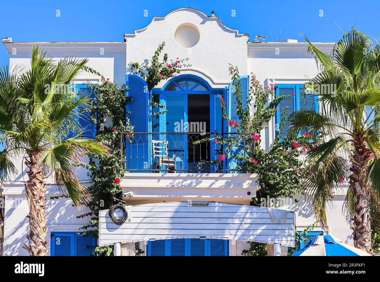 Casa bianca con persiane blu, piante tropicali e palme pittoresche. Destinazione turistica sulla costa dell'Egeo. Foto Stock