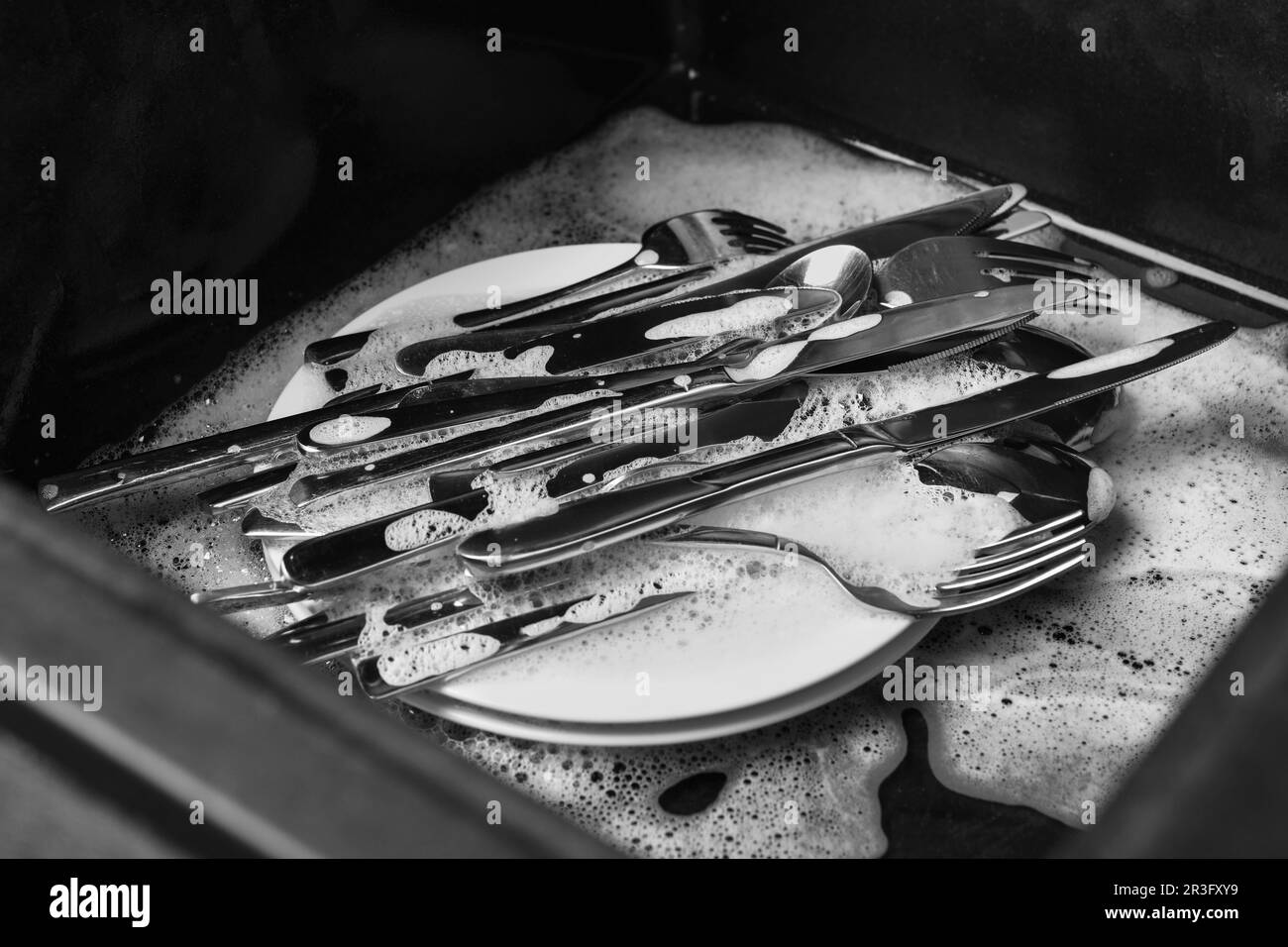 Lavando cucchiai d'argento, forchette e coltelli in lavello da cucina con schiuma Foto Stock