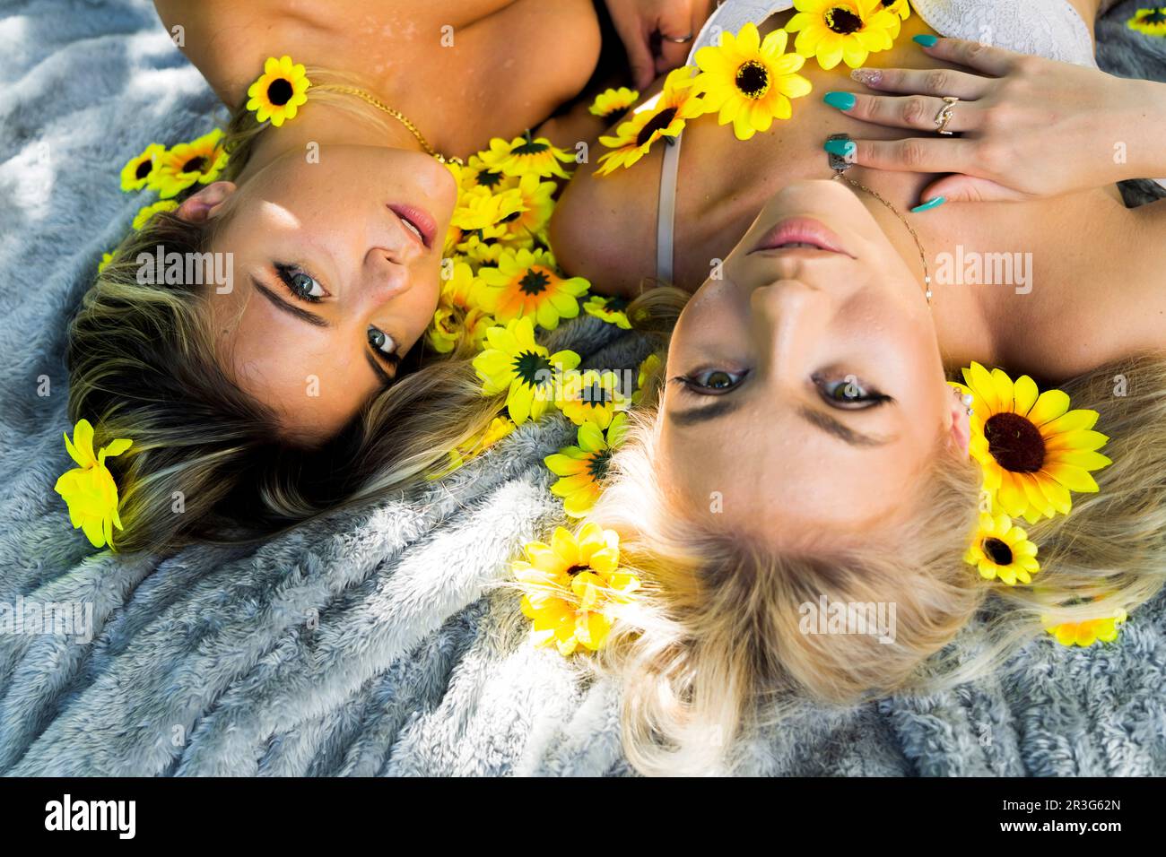 Due splendidi modelli biondi si posano all'aperto con fiori selvatici mentre si gode il clima estivo Foto Stock