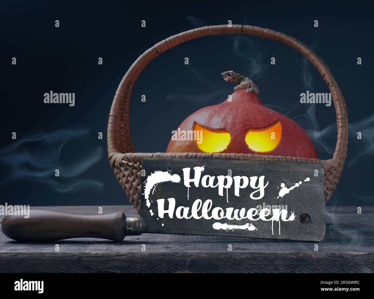 Zucca di Halloween scolpita Jack o lantner in un cesto su un tavolo di legno rustico con un taglio macellaio, spazio per il testo Foto Stock