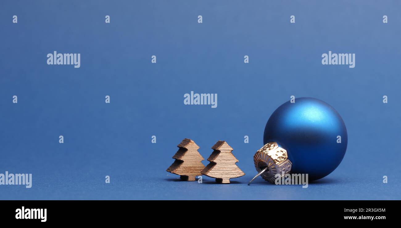 Sfera blu dell'albero di Natale con le piccole forme dell'albero di legno su uno sfondo di carta blu con lo spazio per il vostro testo Foto Stock