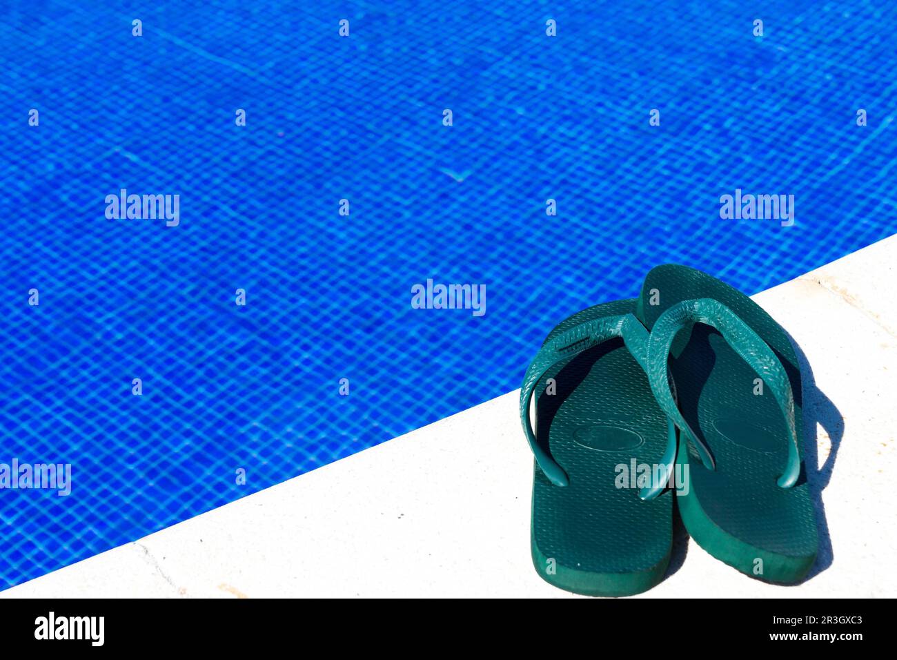 Un paio di pantofole da bagno verdi ai margini di una piscina Foto Stock