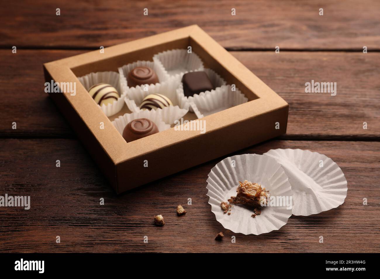 Bicchieri di carta caramella vicino a scatola parzialmente vuota di dolci al cioccolato su tavolo di legno Foto Stock