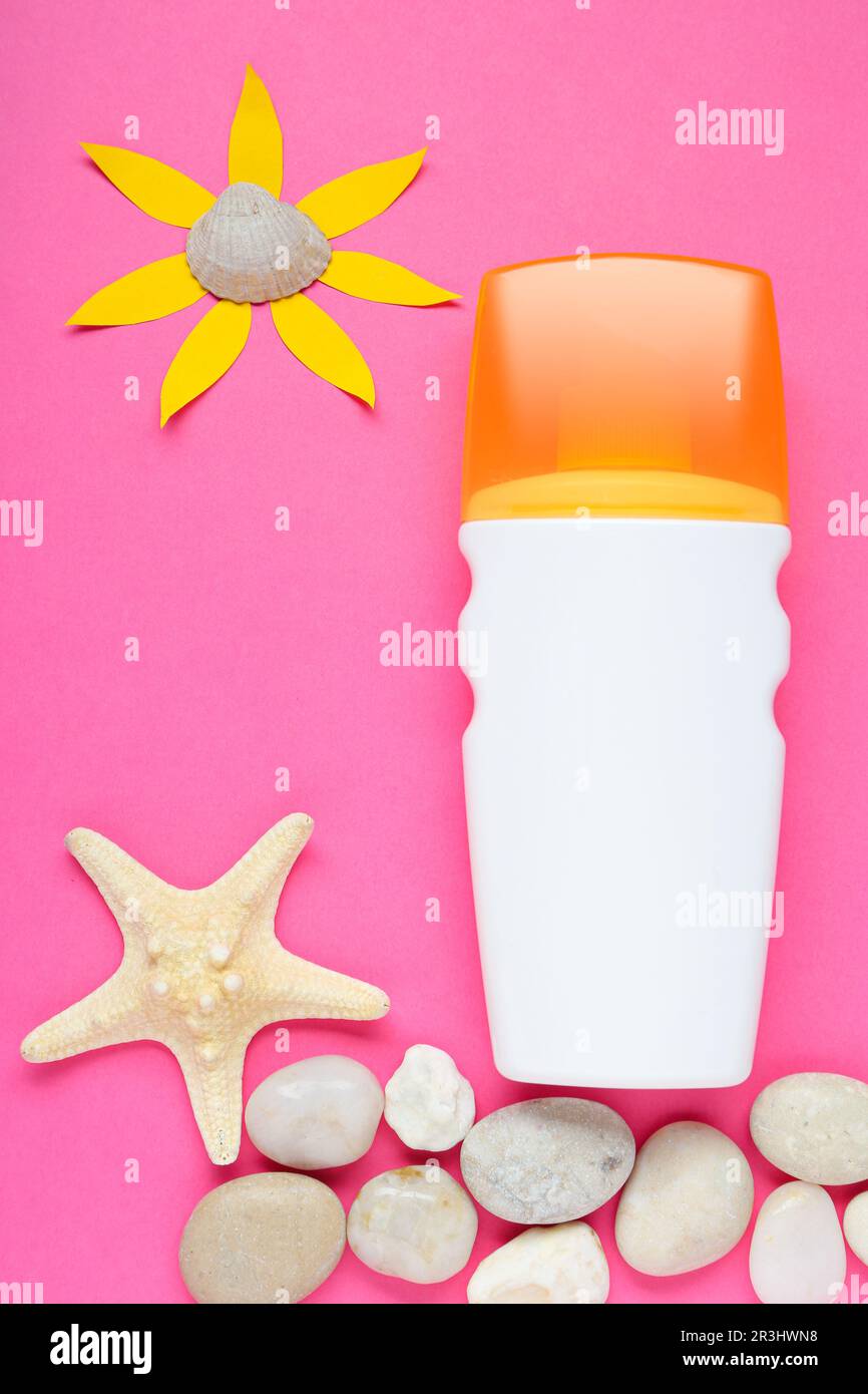 Crema solare, sole di carta e conchiglie su sfondo rosa, giacitura piatta Foto Stock