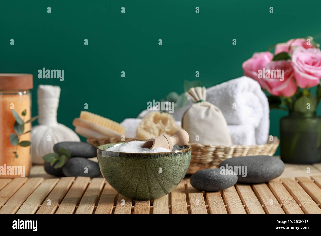 Bella composizione con sale marino, fiori e diversi prodotti termali su tavolo di legno vicino parete verde, spazio per il testo Foto Stock