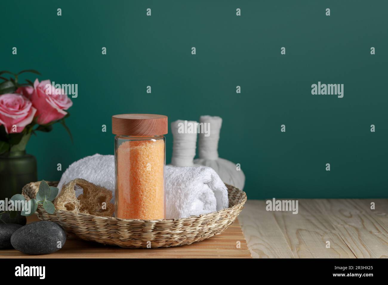 Bella composizione con sale marino, rose e diversi prodotti termali su tavolo di legno vicino parete verde, spazio per il testo Foto Stock