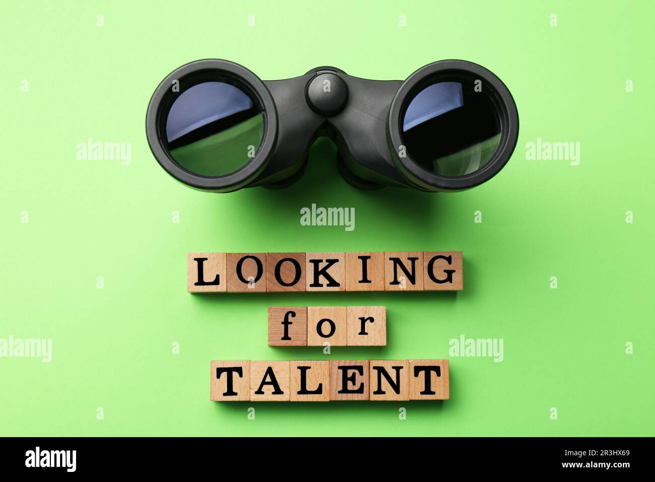 Concetto di reclutamento del personale. Frase cercando talento fatto di cubetti di legno e binocolo su sfondo verde chiaro, piatto Foto Stock