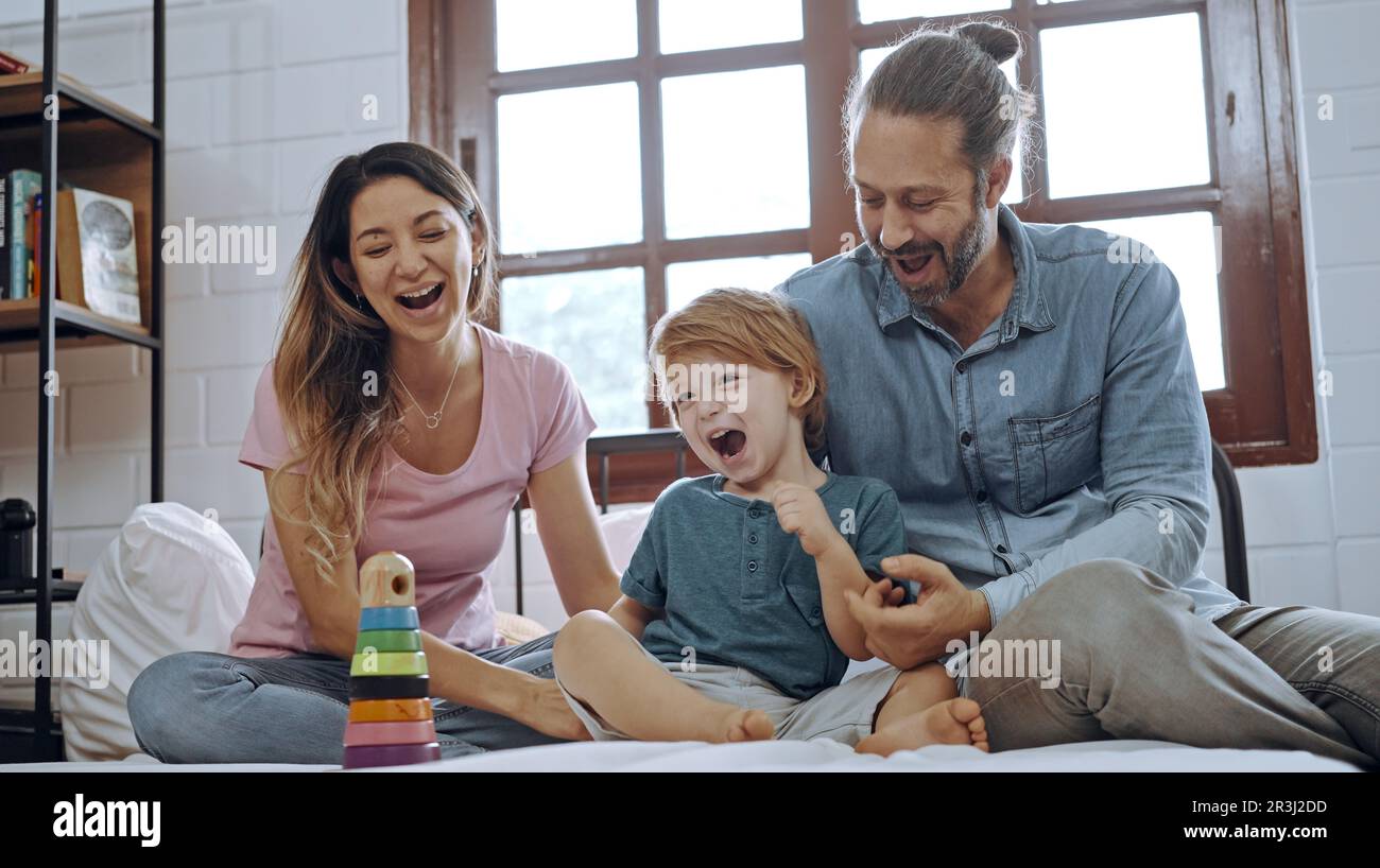 Felicità figlio giocare giocattolo con madre e padre a letto, godere di rilassarsi insieme a casa. Foto Stock