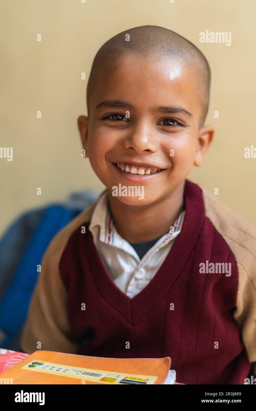 Felice ragazzo indiano seduto in classe, indossando la sua divisa scuola e sorridendo, educazione e concetto di ritorno a scuola. Foto Stock