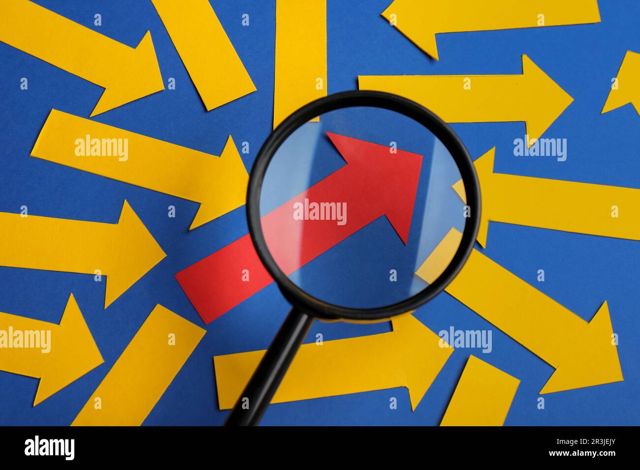 Processo di reclutamento, ricerca dipendente. Vista attraverso la lente d'ingrandimento della freccia di carta rossa tra quelle gialle su sfondo blu, piatto Foto Stock