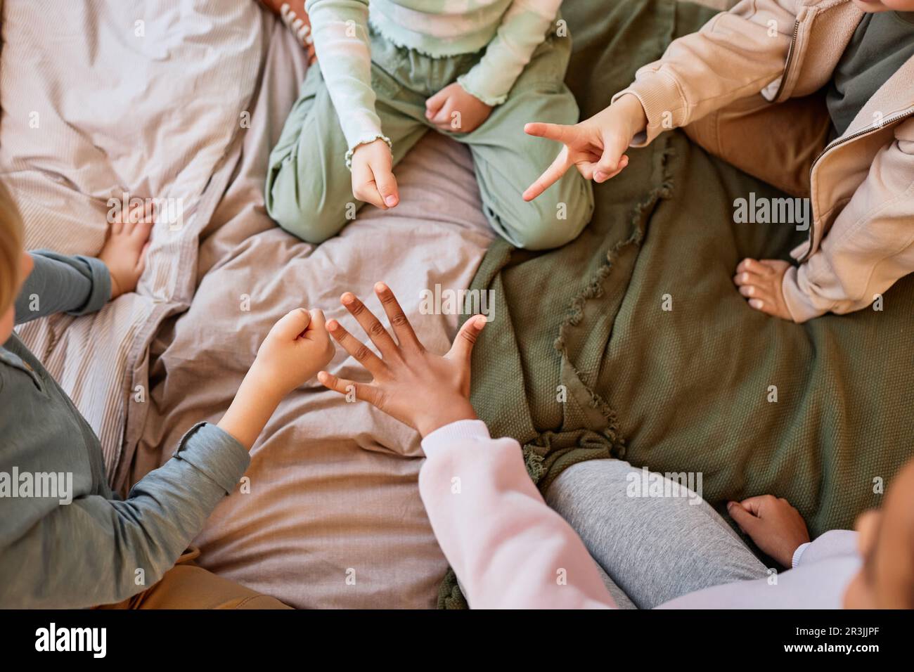 Vista dall'alto primo piano di gruppo di bambini che giocano a forbici di carta rock mentre si siedono sul letto in cerchio, spazio copia Foto Stock