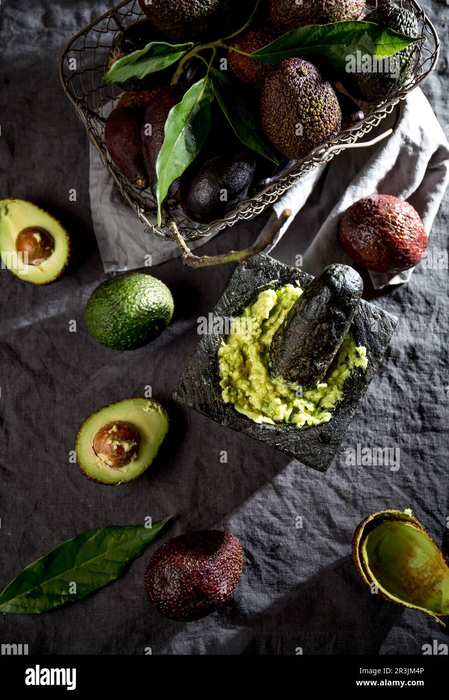 Avocado. Guacamole. Salsa guacamole messicana in mortaio di pietra, cesto completo con avocado, metà avocado su tovaglia di lino. In alto Foto Stock