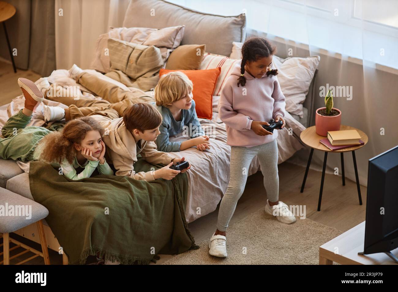 Vista ad angolo alto di un gruppo di bambini che giocano insieme a videogiochi e sdraiati sul letto, spazio copia Foto Stock