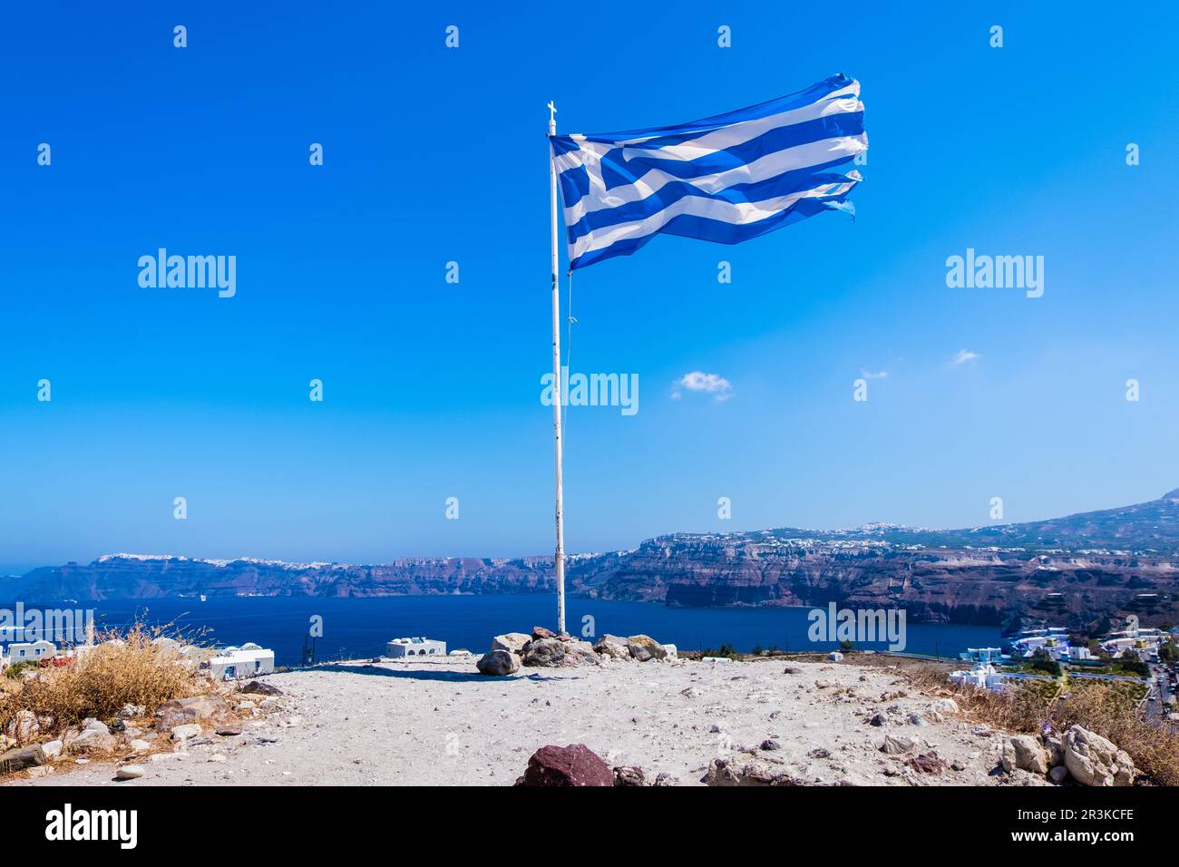 Bandiera greca che sventola sulla cima di una collina con il mare e l'isola di Santorini sullo sfondo Foto Stock