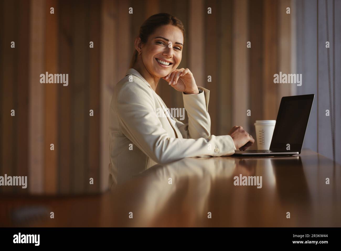 Donna d'affari caucasica che guarda la macchina fotografica mentre si siede in un bar. Una donna felice che lavora in remoto in una caffetteria. Foto Stock
