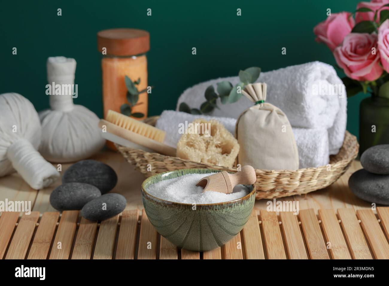 Bella composizione con sale marino, fiori e diversi prodotti termali su tavolo di legno vicino parete verde Foto Stock