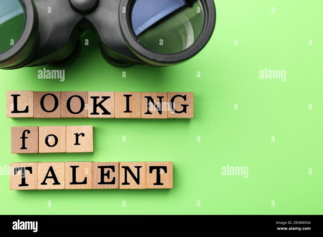 Concetto di reclutamento del personale. Frase cercando talento fatto di cubi di legno e binocoli su sfondo verde, piatto. Spazio per il testo Foto Stock