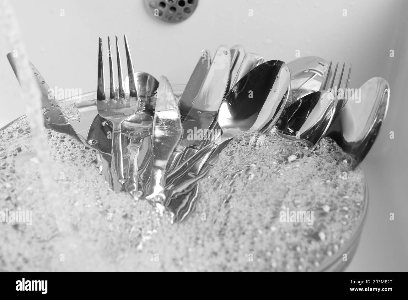 Lavare cucchiai d'argento, forchette e coltelli sotto il flusso d'acqua in lavello da cucina, primo piano Foto Stock