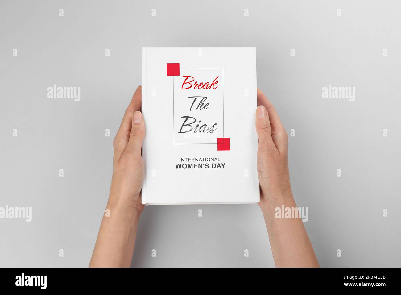 Libro di tenuta della donna con titolo Break the Bias dedicato alla Giornata internazionale della donna contro sfondo grigio chiaro, primo piano Foto Stock