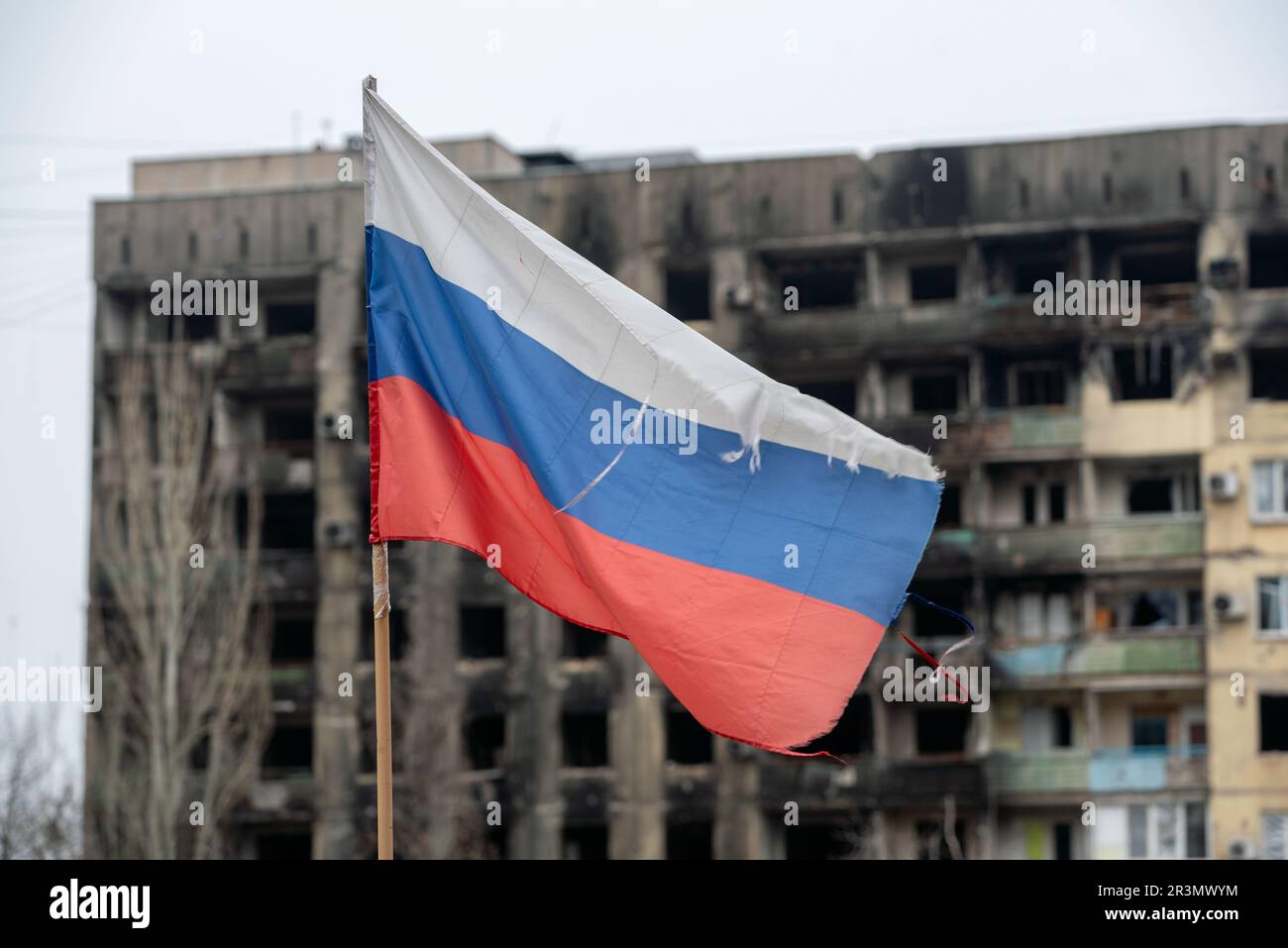 Bandiera tricolore della Russia sullo sfondo di case distrutte e bruciate in Ucraina Foto Stock