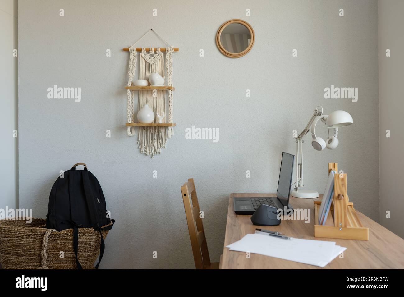 Interno di camera minimalista con borsa per studenti e tavolo in legno con sedia e computer portatile vicino alla finestra in appartamento moderno Foto Stock