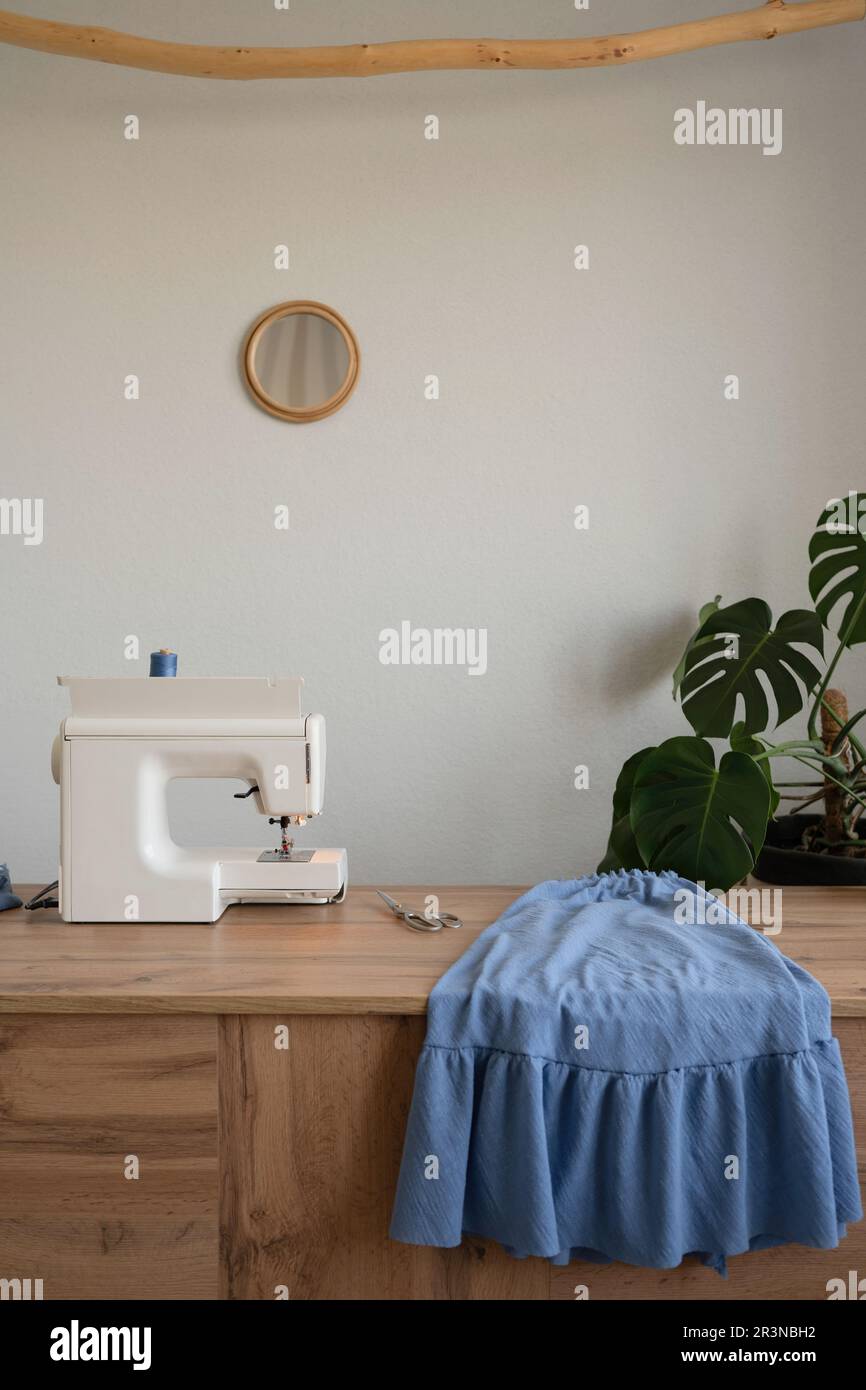 Macchina da cucire contemporanea posta su un tavolo di legno vicino a tessuto blu in atelier creativo chiaro Foto Stock