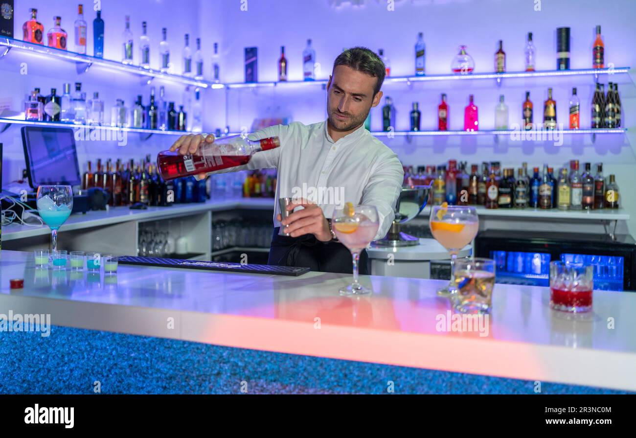 Barista giovane maschio concentrato guardando verso il basso e versando l'alcool dalla bottiglia nel jigger mentre preparano le bevande del cocktail e si levano in piedi in piedi nel banco Foto Stock