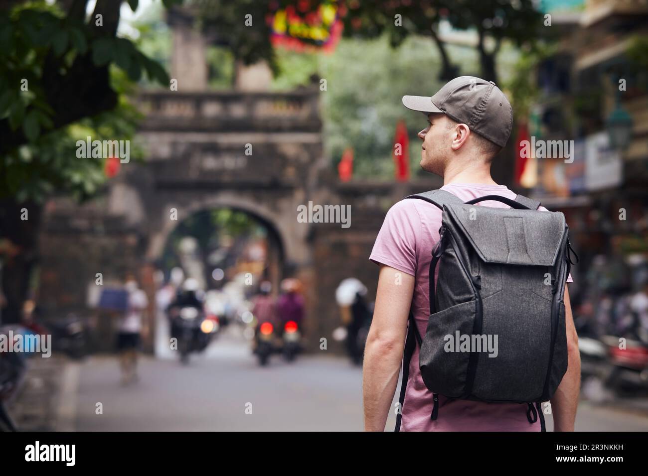 Il viaggiatore cammina sulla trafficata strada asiatica. Vista posteriore di uomo con zaino nel centro storico di Hanoi, Vietnam. Foto Stock
