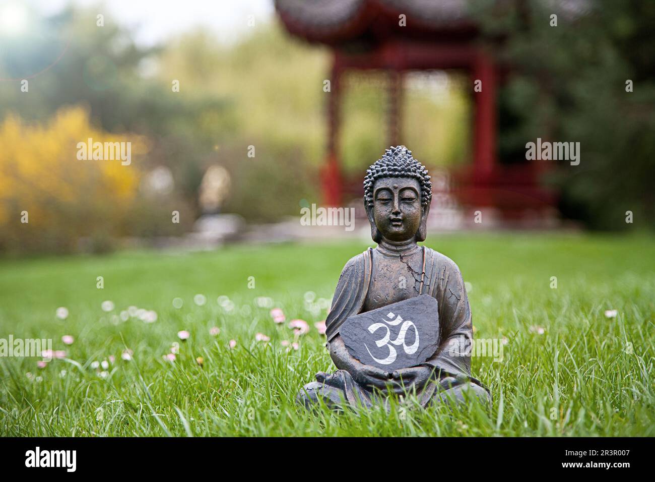Statua del Buddha seduta su un prato con un cartello che riporta il simbolo Om Foto Stock