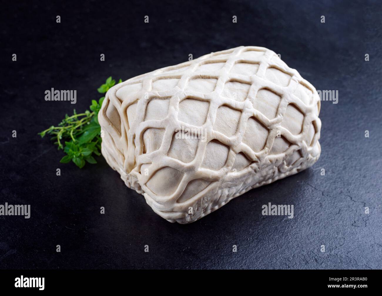 Bistecca di maiale grezza Kasseler come pezzo di pasta sfoglia, come primo piano offerto su una tavola nera con erbe aromatiche Foto Stock